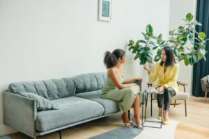 Two women sharing a conversation in a stylish living room with plants.