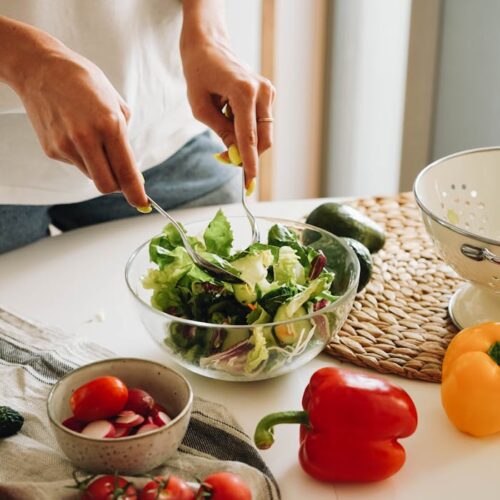 A person mixes a fresh vegetable salad with tomatoes and bell peppers in a kitchen.